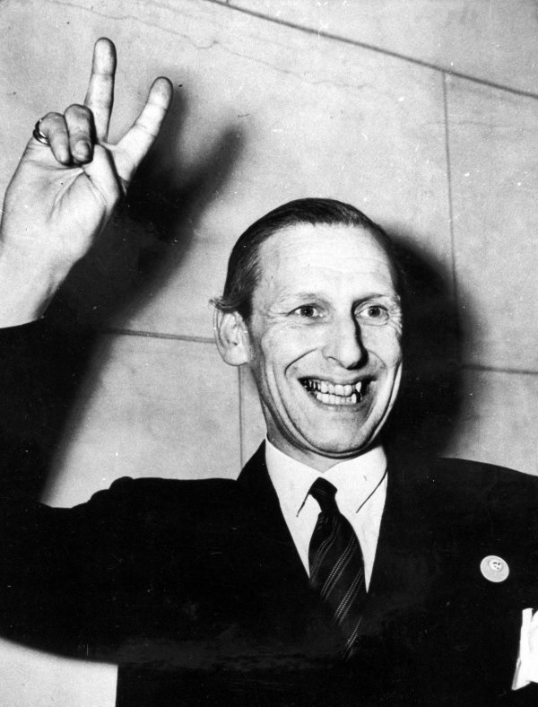 De Laveleye - A black and white photo of a man in a dark suit and tie making the V for Victory sign