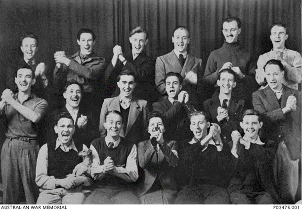 Black and white photo of a group of people in war time dress. All smiling